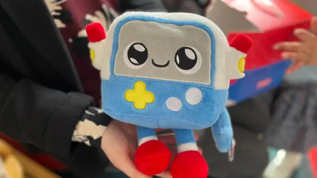 Gabbo這款絨毛玩具被人拿在手中。它的質地柔軟，如同泰迪熊，但外型帶有機器人特徵