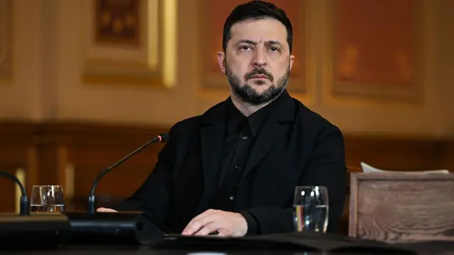 Зеленський сидить за столом перед мікрофоном