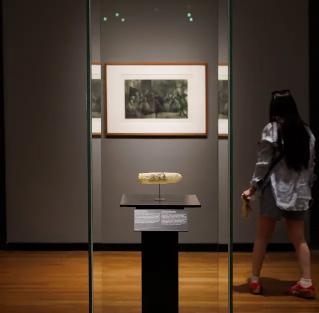 A visitor at the Rijksmuseum walks past a glass case containing the condom, which is presented on a metal plate with a sign including more information about it below.