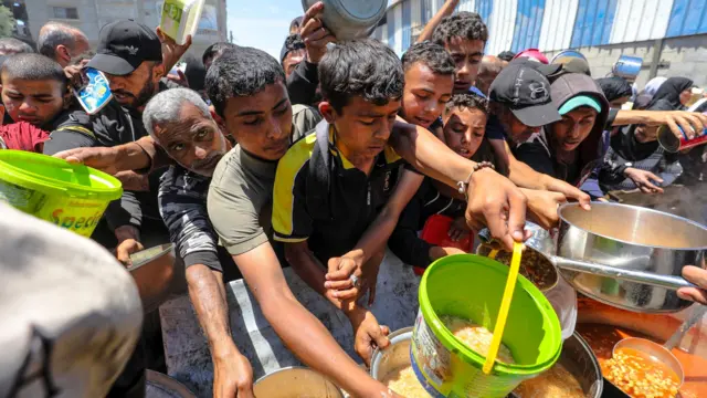 فلسطينيون جائعون نازحون يهرعون إلى مطبخ توزيع الطعام، ويمددون حاوياتهم الفارغة لاستلام الطعام في غزة، الأراضي الفلسطينية، في 7 مايو/أيار 2025. أصدرت الأمم المتحدة "تحذيرًا صارمًا" بعد شهرين من الحصار الإسرائيلي شبه الكامل لغزة، حيث يعاني القطاع من شحّ الغذاء و"يتصارع الناس على الماء وسط قصف متواصل". 