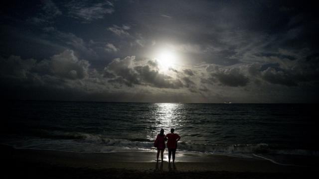 Duas pessoas observam eclipse a partir da praia