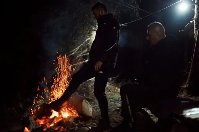 Muškarac nogom rasipa vatru tokom noći da se ugreje