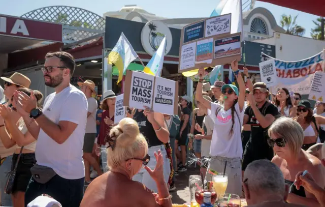 Para demonstran menentang pariwisata massal di depan para turis yang sedang duduk di teras restoran, di Kepulauan Canary, Spanyol, pada 20 Oktober 2024.