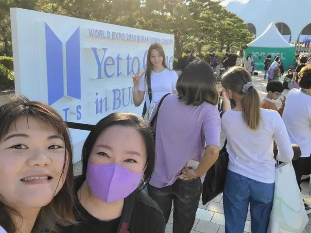 아미들이 한 공연장 앞에서 포즈를 취하며 사진을 찍고 있다