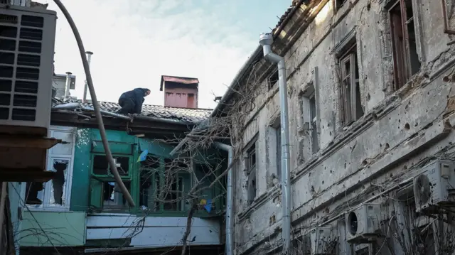 یک مرد روی سقف خانه مشغول بررسی خسارت پس از اصابت موشک به خانه است