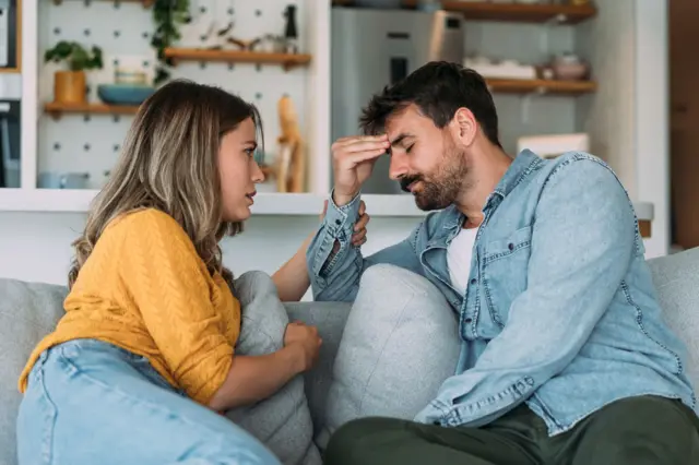 رجل وامرأة يجلسان على أريكة يبدو أن الرجل متعب إذ يضع يده على رأسه بينما تبدو الزوجة في محاولة لمواساته.