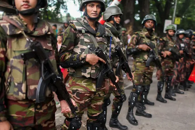 কিছু সেনাসদস্য অস্ত্র হাতে রাস্তায় দাঁড়িয়ে আছেন