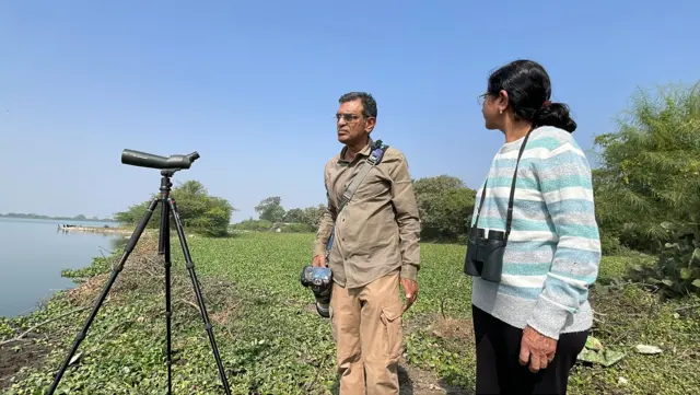 રાજકોટના ઇશ્વરીયા તળાવમાં જળકુંભીથી છવાયેલા કાંઠા પર 25 નવેમ્બર, 2025ના રોજ પક્ષી નિરીક્ષણ કરી રહેલાં પક્ષી નિરીક્ષક અશોક મશરૂ અને તેમનાં પત્ની ભાવનાબહેન મશરૂ 