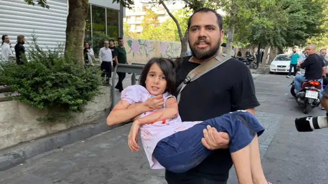 A man carries a wounded girl, who has blood on her shirt and body, following an Israeli airstrike in central Tehran, Iran, on 15 June 2025.