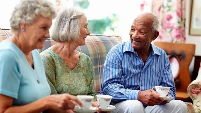 ሁለት አረጋውያን ሴቶች ከአዛውንት ወንድ ጋር ቁጭ ብለው ሲጫወቱ