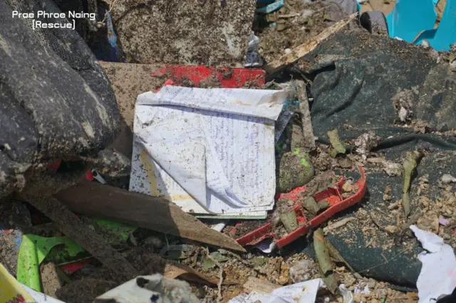 လွင့်စင်ပြန့်ကြဲနေတဲ့ ကျောင်းသုံးဗလာစာအုပ်တစ်အုပ်၊ ကျောင်းစိမ်းဝတ်စုံ၊ ကွန်ပါဘူး အနီရောင် 