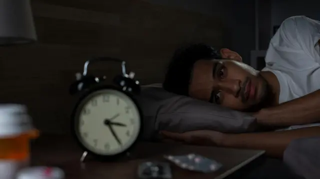 Homem deitado na cama à noite, acordado, olhando para o despertador que marca 3h25.