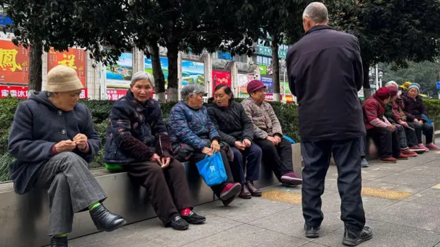 Grupo de idosos sentados em um banco público, conversando em uma área urbana de Chongqing, no sudoeste da China, em março de 2025