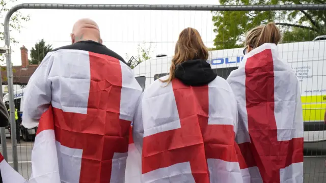 Três pessoas de costas envoltas na bandeira da Inglaterra