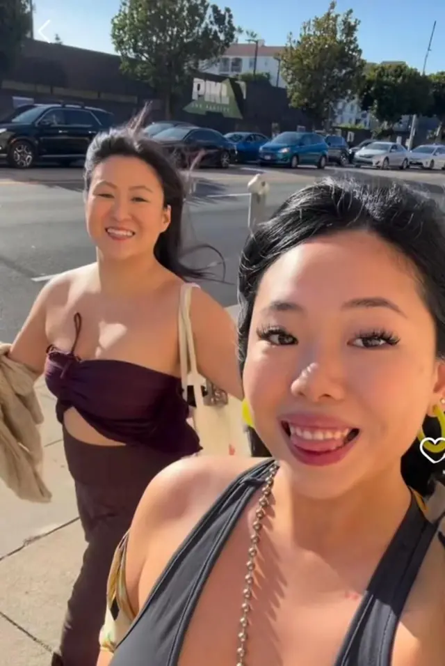 Ambas amigas caminan por una calle con vestidos elegantes y sonriendo a la cámara.