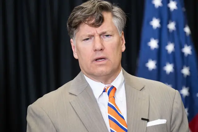 O subsecretário do Departamento de Estado americano, Christopher Landau, durante coletiva de imprensa em 12 de maio de 2025. Ele veste terno bege e gravata listrada de laranja, azul e branco e está no meio de uma fala