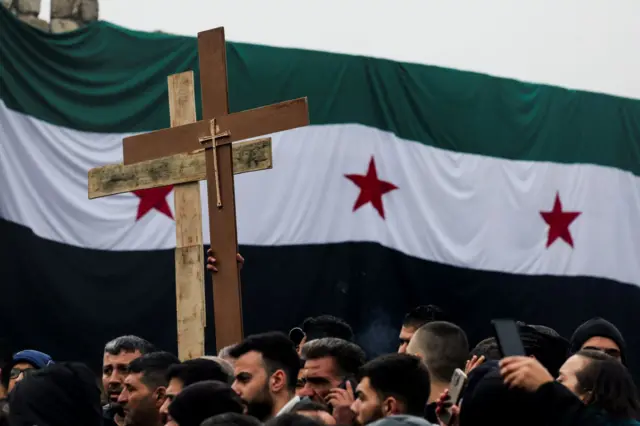 Şam'da Hristiyanların düzenlediği protestoya katılanlar. Yeni Suriye bayrağının önünden ellerinde haçla ilerliyorlar.  