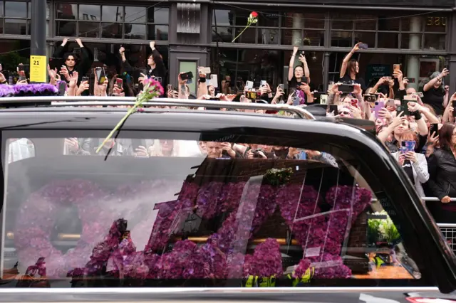 El carro fúnebre en el que transportaban el ataúd de Ozzy, mientras fanáticos les toman fotos.