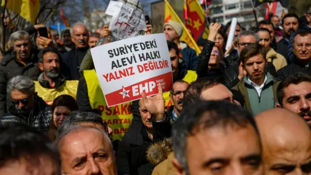 Kalabalık, bir pankartta "Suriye'deki Alevi halkı yalnız değildir" yazıyor.