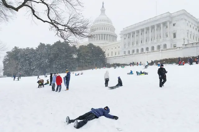 25 Ocak 2026'da Washington'daki Capitol Hill'de kar fırtınası sırasında bir çocuk kardan melek yapıyor, kızakçılar ise yanından geçiyor.