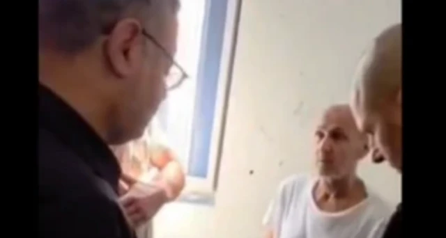 Kötü kalite bir görüntüde iki kişi bir cezaevi hücresinde karşılıklı konuşuyor