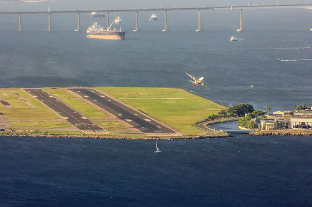 Avião próximo da pista do Santos Dumont, rodeada pela Baía de Guanabara e com a Ponte Rio-Niterói ao fundo