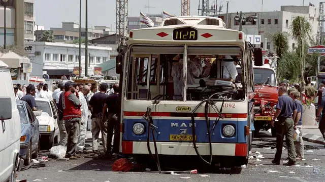 Люди стоят вокруг взорванного автобуса