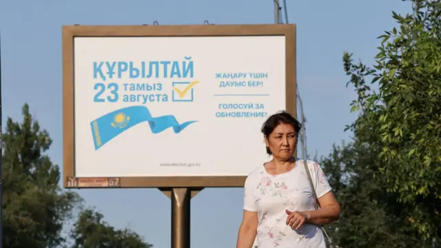 билборд с текстом о выборах Курултая и женщина перед ним