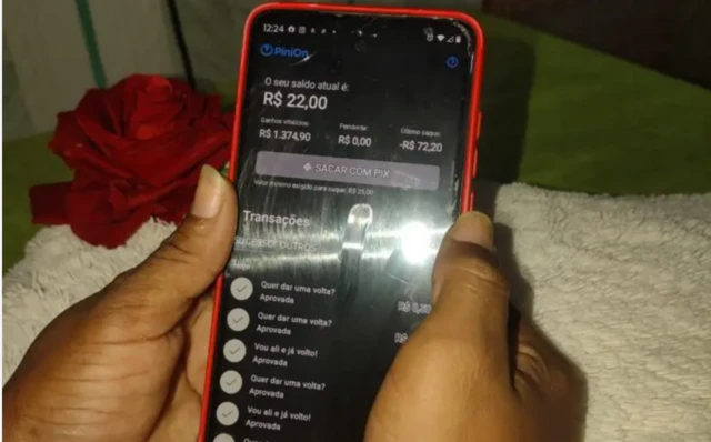 Duas mãos seguram um celular que mostra a tela de um aplicativo de microtarefas, com o saldo do usuário
