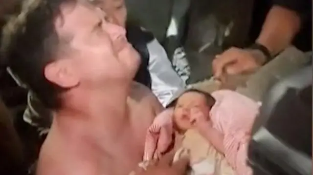 Momento em que o bebê é resgatado e pai o pega no colo
