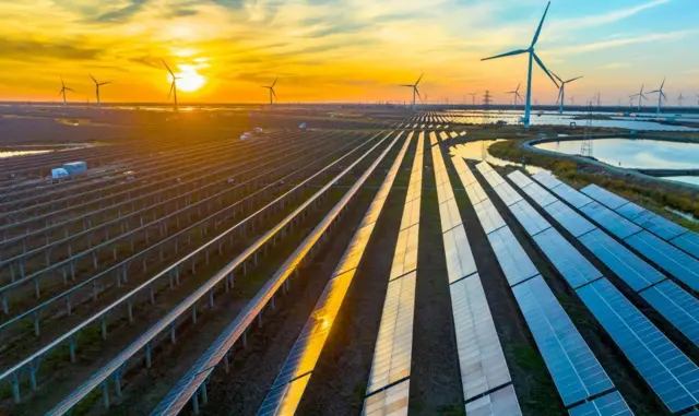 Paineis foltovoltaicos e torres de energia eólica são vistos em campo