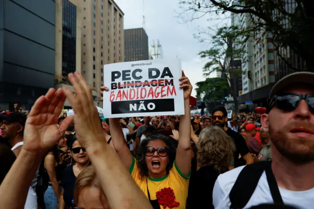 Protesto contra PEC da Blindagem na Avenida Paulista, no domingo (21/09). No centro, no meio de uma multidão, está uma mulher usando camiseta amarela da seleção brasileira segurando um cartaz 'Pec da Blindagem Não', com a palavra Blindagem riscada e substituída por 'Bandidagem'
