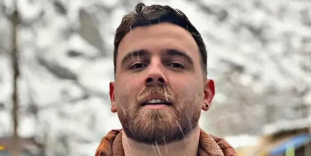 Imagem de comerciante de 26 anos, com cabelo curto e barba e uma roupa de frio, do pescoço pra cima