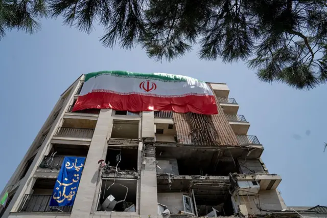 ইসরায়েলের হামলায় ক্ষতিগ্রস্ত একটি ভবনে ঝুলছে ইরানের পতাকা