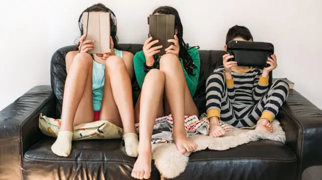 Trois enfants assis sur un canapé, le visage collé à l'écran