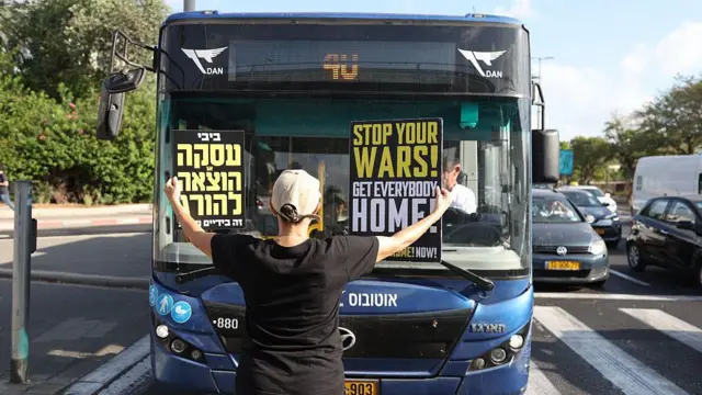 Человек с плакатами в руках стоит перед автобусом на проезжей части