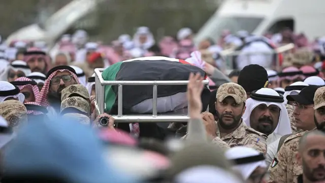 Kuveyt'te bir askeri cenazede askerler ve yerli kıyafetli halk bir arada. Tabut omuzlarda taşınıyor.