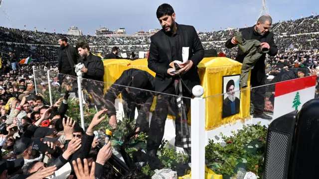 مشاركون في مراسم تشييع الأمينين العامين السابقين لحزب الله حسن نصر الله وهاشم صفي الدين يلقون رموزاً لمسؤولي الأمن لوضعها على النعشين 