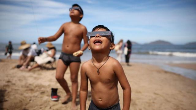 Meninos de pele bronzeada e óculos de eclipse em praia 