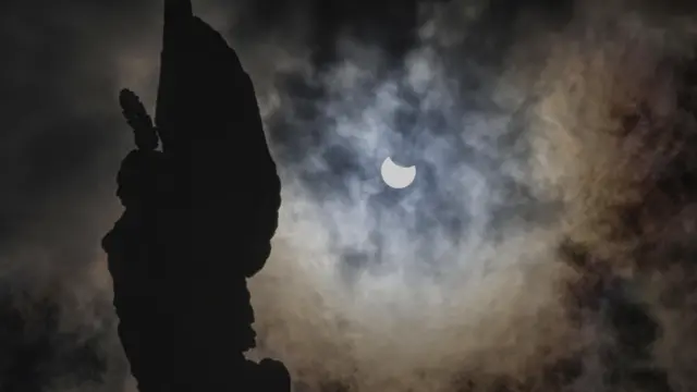 سایه یک شئ در کنار آسمان ابری و دایره ناکامل خورشید