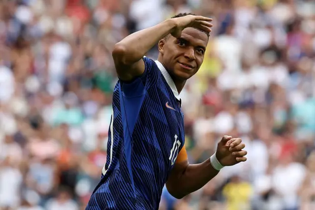 Kylian Mbappé akoze ikimenyetso n'ikiganza ku mutwe yishimira gutsinda igitego cya mbere cy'ikipe ye y'Ubufaransa mu mukino wo guhatanira umwanya wa gatatu mu gikombe cy'isi cya 2026 wayihuje n'Ubwongereza, ku kibuga cya Miami, muri leta ya Florida muri Amerika, ku itariki ya 18 Nyakanga (7) mu mwaka wa 2026.
