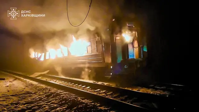 В темряві палає вагон потяга. Вогонь вихоплюється з вікон, здіймається густий дим. Уздовж вагону тягнуться залізничні колії, на землі видно сліди від снігу. 