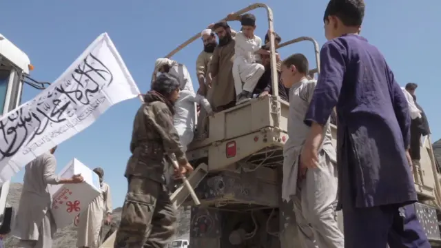 پشت یک وسیله نقلیه روباز پر از جمعیت. شخصی که پرچمی سفید با نوشته‌های سیاه در دست دارد پشت کامیون ایستاده است