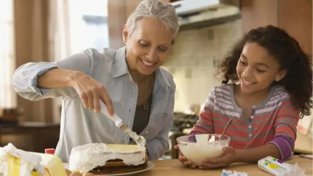 Mulher mais velha e menina cozinham juntas e confeitam um bolo