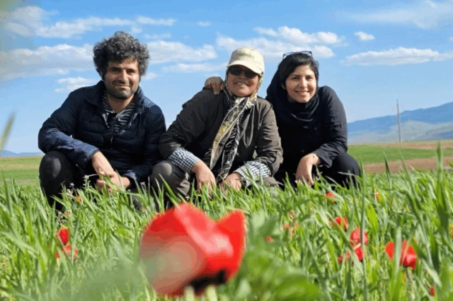 درې کسان، یو سړی او دوه ښځې، په زرغون او سمسور ډګر کې چې سره ګلان پکې دي، کیناستي دي، او شا کې غرونه ښکاري. ښځې دودیزې جامې اغوستي دي.