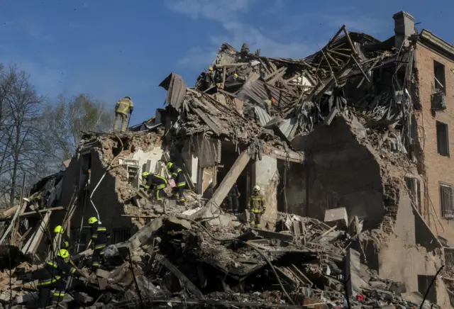 Дом, часть которого полностью разрушена; на руинах работают несколько спасателей.