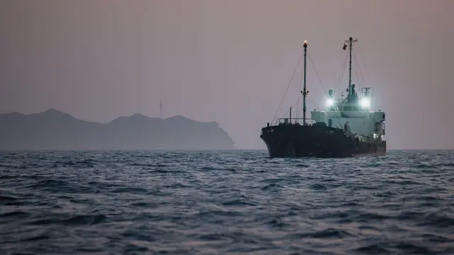 Hürmüz Boğazı'ndan geçen bir tanker ışıklarını yakmış durumda ilerliyor. Hava yeni kararmak üzere