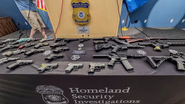 Una serie de armas en una mesa con las siglas de la oficina de Investigaciones del Departamento de Seguridad Nacional de EE.UU.