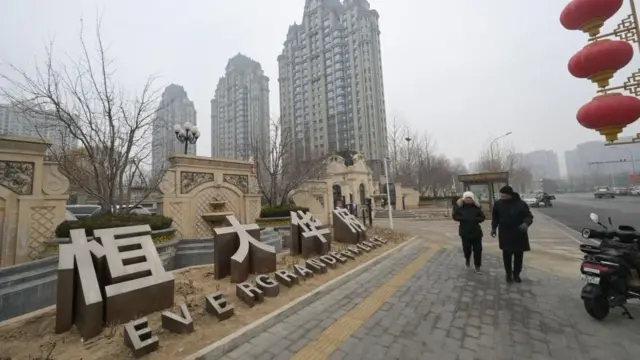 2024年1月30日、霧の多い曇り空の北京で、コートと帽子を身につけた人々が恒大が開発した集合住宅の前を通り過ぎている