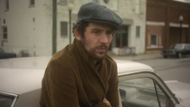 Josh O'Connor in 1970s flat cap and brown coat in a still from The Mastermind